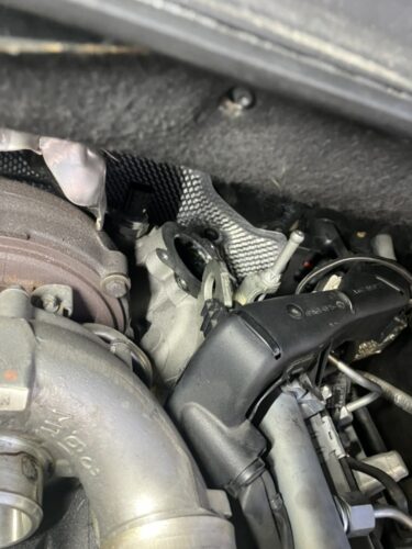 ベンツGLクラス エンジンチェックランプ修理 EGRバルブ交換作業 エンジンルーム メルセデスベンツGLクラスのエンジンルームで、EGRバルブを取り外した状態の写真。排気系周辺のパイプやターボ付近が見えており、EGRバルブ交換作業中の様子が確認できる整備中の状態。