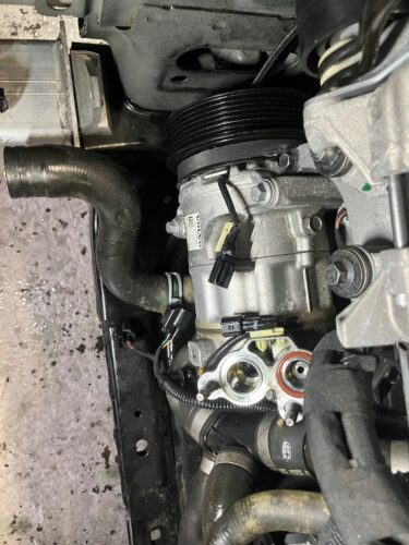 交換作業中のボルボV60のエアコンコンプレッサー。冷却系ホースや配管を取り外し、新品コンプレッサーを取り付ける直前の状態を撮影した整備風景。